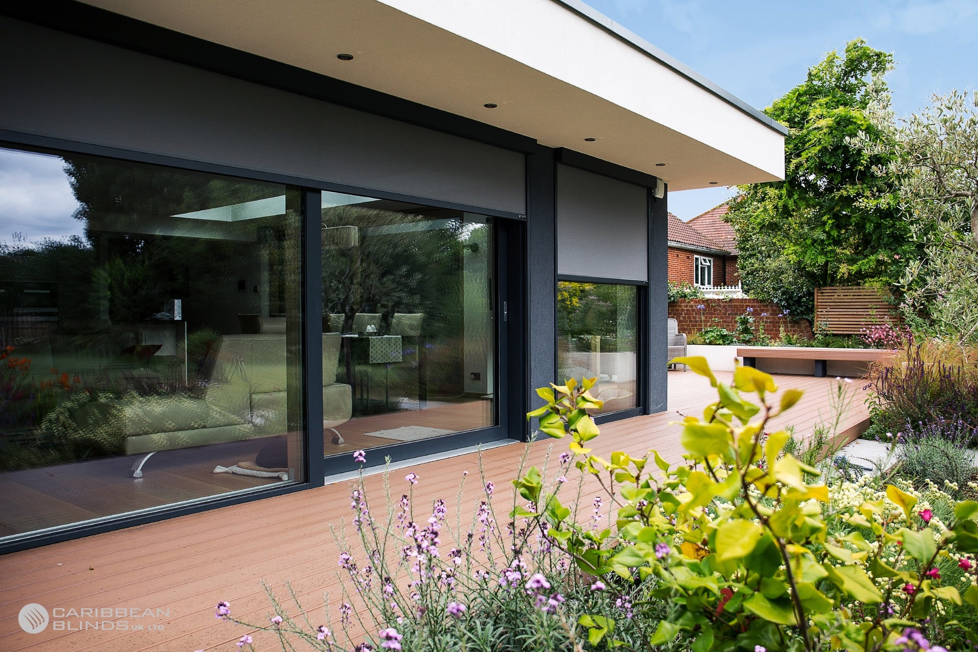 Modern house with large glass windows and a garden with flowers and trees.