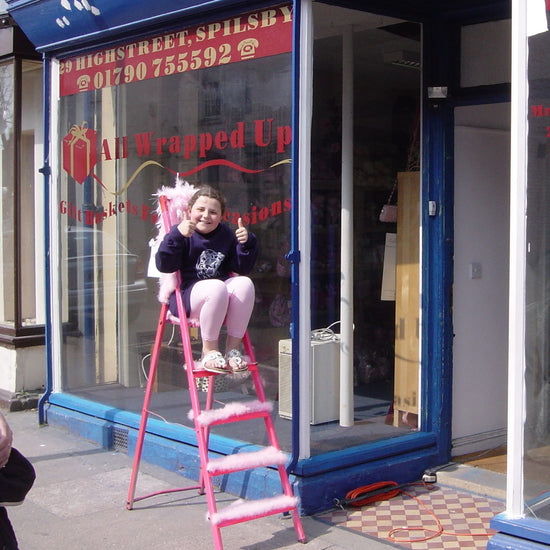 Happy child sitting on a ladder in front of a shop window